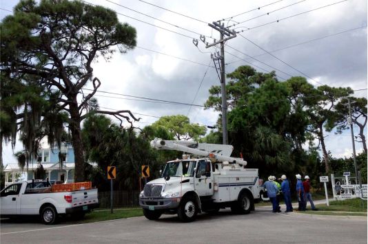 Truck next to a power line, with several workers standing next to it.