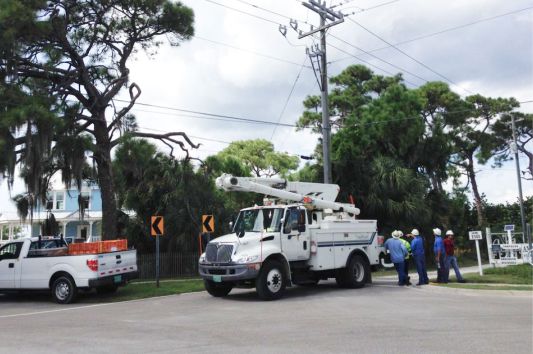 Truck next to a power line, with several workers standing next to it.